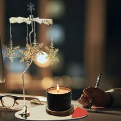 a person writing on a paper next to a candle and computer screen with snowflakes