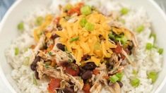 a white bowl filled with rice, beans and shredded cheese topped with green onions on top