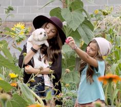 two girls are standing in a field with sunflowers and one girl is holding a small white dog