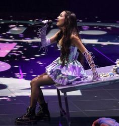 a woman sitting at a table with a microphone in her hand while singing on stage