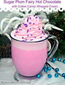 a pink frosted drink with sprinkles in a glass mug next to christmas decorations