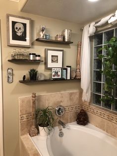 a bath tub sitting next to a window with pictures on the wall above it and plants