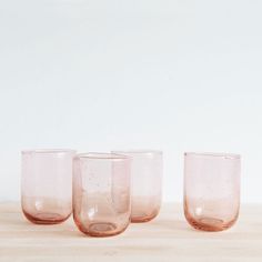 four pink glass cups sitting on top of a wooden table next to eachother