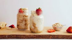 three jars filled with oatmeal and strawberries on top of a cutting board