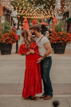 a man and woman kissing on the street in front of some buildings with christmas lights