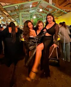 three beautiful women posing for the camera in front of a group of people at a party