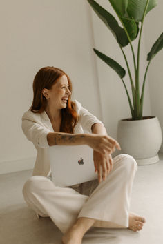 a woman is sitting on the floor with her laptop in front of her and smiling