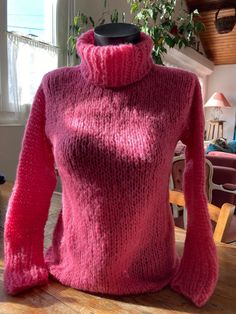 a pink sweater sitting on top of a wooden table next to a potted plant