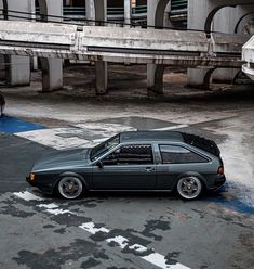 a car parked on the street in front of an overpass with another car behind it