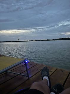 a person is sitting on a dock with their feet propped up in front of the water