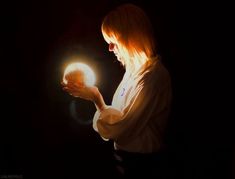 a woman holding a glowing ball in her hand with light shining on her face and hair