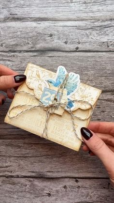 two hands holding an old fashioned envelope with paper and twine tied to it on wooden planks