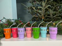 six colorful cups with straws in front of a christmas tree