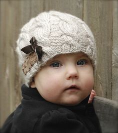 a baby wearing a knitted hat with a brown bow on it's head