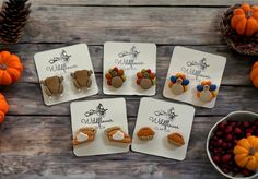 six thanksgiving themed earrings sitting on top of coasters next to berries and pine cones