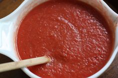 a white bowl filled with red sauce on top of a wooden table next to a wooden spoon