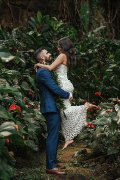 a pregnant woman in a white dress is holding her husband's back as they walk through the jungle