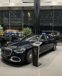 a black car parked in front of a building with glass walls and lights on it