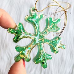 a green and white snowflake ornament being held by someone's hand