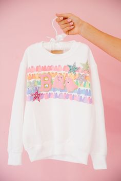 Get ready to spook up some fun with our MINI KIDS STAR GHOULS PULLOVER! This white pullover features a vibrant rainbow striped ghosts design and playful pink letters B and pink ghosts as O's that spell "Boo". Complete with colorful resin star patches, this pullover is perfect for your little one to show off their unique and quirky style. It's a boo-tiful addition to any wardrobe! All orders are currently shipping within 14 business days. To receive item quicker, expedited shipping is available a Star Patches, Pink Letters, Boo Tiful, Quirky Style, White Pullover, Pink Letter, Ghost Design, Letter B, Rainbow Stripes