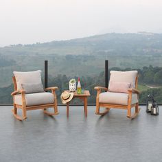 two wooden chairs sitting on top of a patio next to a table with a cup