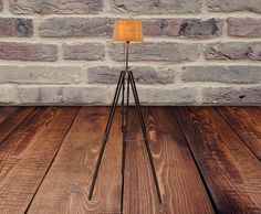 a floor lamp with a yellow shade on it in front of a brick wall and wooden floor