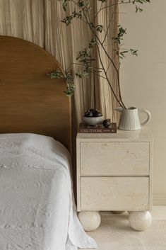 a white bed sitting next to a wooden dresser with a potted plant on top