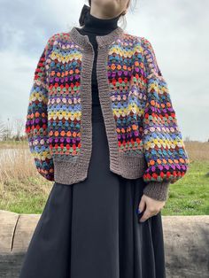 a woman in a black dress and colorful crochet jacket