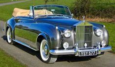 an old fashioned car is parked on the side of the road in front of a grassy field