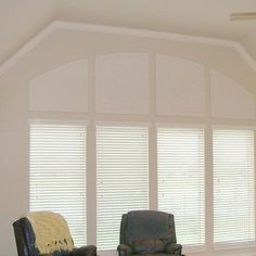 two chairs sitting in front of large windows with white shutters on each side and one chair facing the other