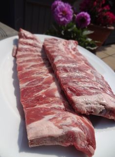 two pieces of raw meat on a white plate with purple flowers in the back ground