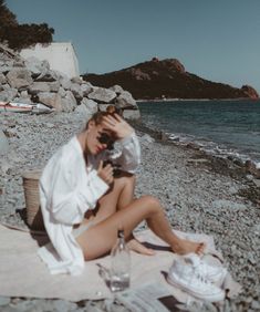 a woman sitting on top of a beach next to the ocean talking on a cell phone