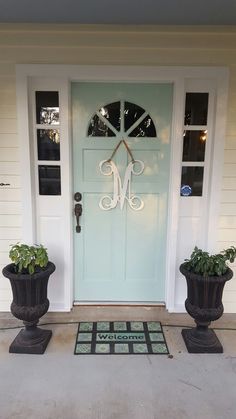 two large planters sitting in front of a door with the letter m on it