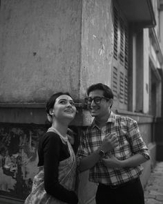 a man and woman standing next to each other in front of a building with shutters