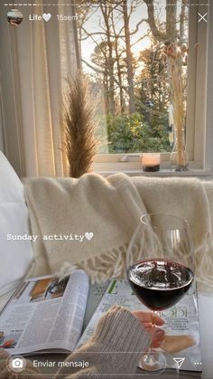 a glass of wine sitting on top of a table next to an open book and magazine