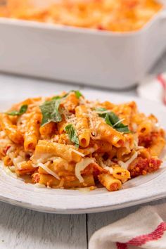 a white plate topped with pasta and sauce next to a casserole dish on a wooden table