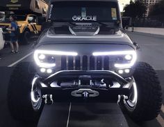 a jeep is parked in a parking lot with its lights on and people walking around