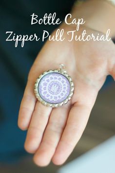 a person's hand holding a purple and white ring with the words bottle cap zipper pull