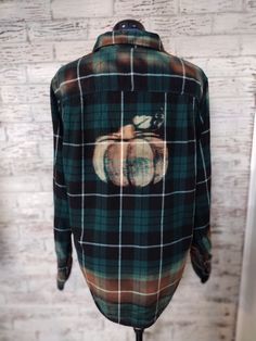 a green and black plaid shirt with an apple on the front, sitting on a stand