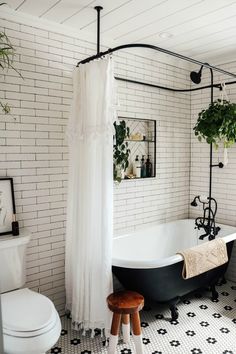 a black and white tiled bathroom with a claw foot bathtub, shower curtain, potted plant and stool