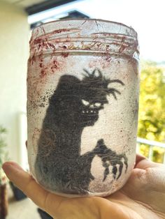 a person holding up a jar with a drawing on it in front of a window