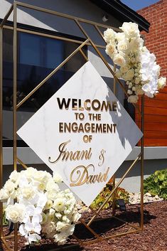 a welcome sign with white flowers in front of a brick building that says, welcome to the engagement of amani and david