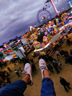 the feet of a person standing in front of an amusement park with ferris wheel and carnival rides