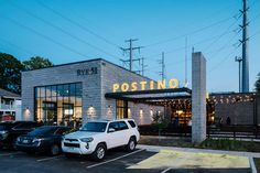 two cars are parked in front of a postino restaurant at dusk with the lights on