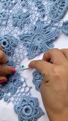 two hands crocheting the edges of a blue lace doily with scissors and thread