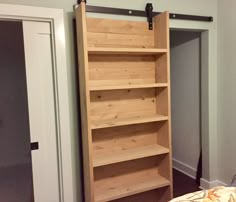 a bed with a wooden book shelf next to a white door in a room that has gray walls and wood flooring