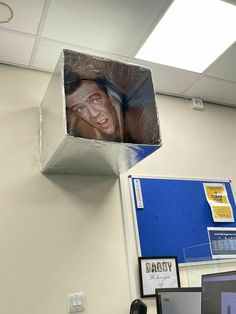 an office cubicle with a cardboard box hanging from it's ceiling and the face of a man sticking out