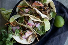 three tacos with meat, onions and cilantro on a plate next to limes