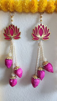 pink and gold earrings with pearls hanging from the side on a white wall next to yellow flowers