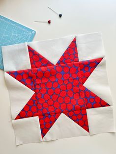 a red and blue star is on the table next to some sewing needles, scissors and thread